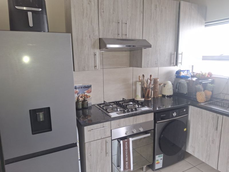 Modern kitchen featuring light wood-grain cabinetry, granite countertops, a gas hob, built-in oven, extractor fan, and integrated laundry appliance space.