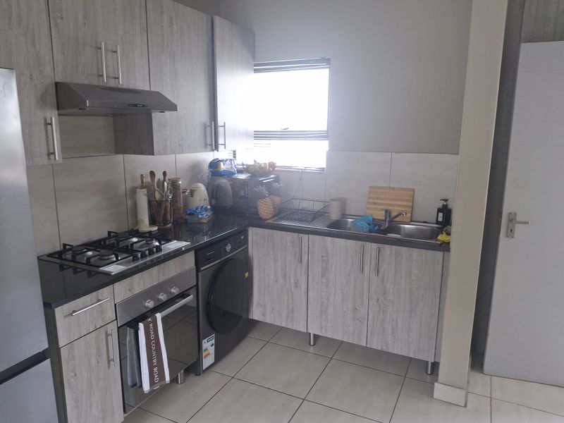 A functional kitchen featuring light wood-grain cabinetry, granite countertops, a gas hob, an electric oven, and a double sink with tiled flooring.