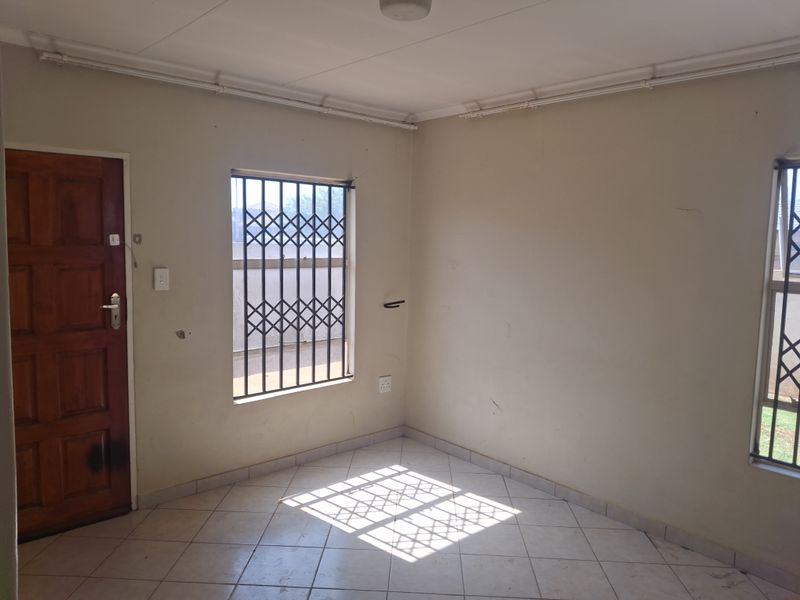 An empty living area featuring tiled flooring, security bars on windows, and a timber entrance door, requiring cosmetic updates to walls and finishes.