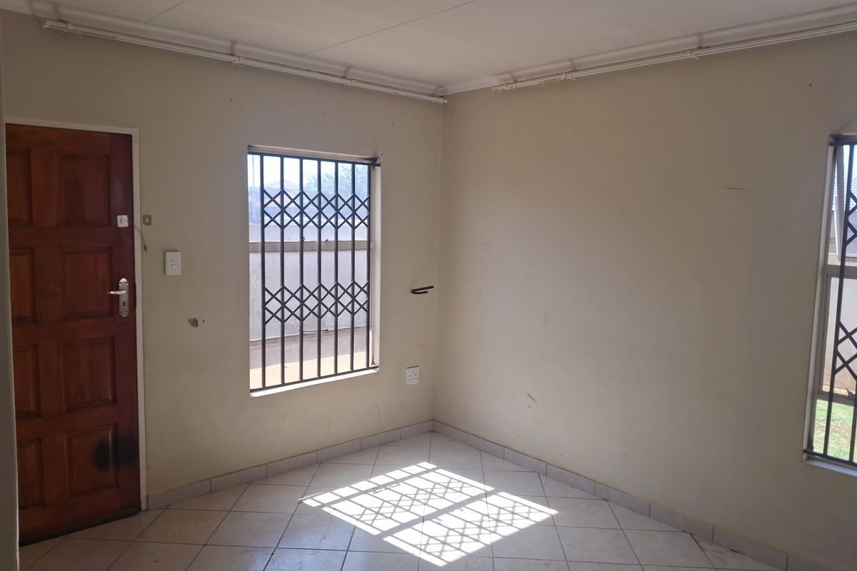 An empty living area featuring tiled flooring, security bars on windows, and a timber entrance door, requiring cosmetic updates to walls and finishes.
