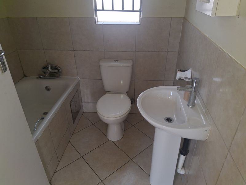 A functional bathroom featuring a pedestal basin, toilet, and built-in bathtub with neutral wall and floor tiling.