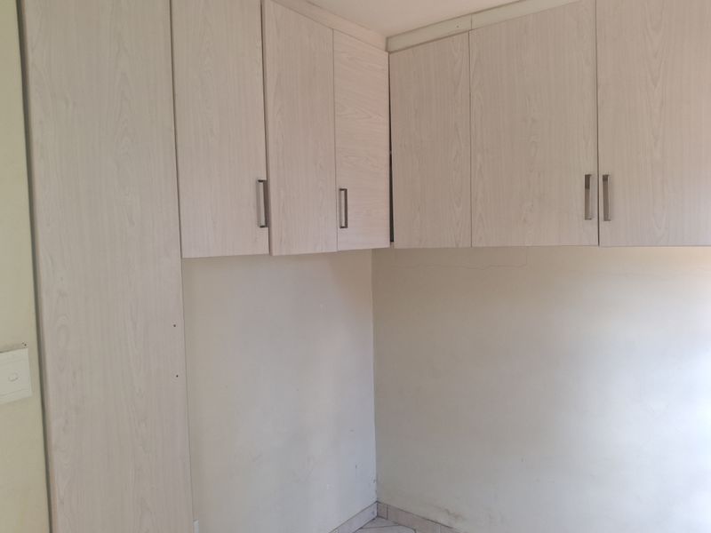 A compact kitchen area featuring light wood-finish built-in cabinetry and tiled flooring, presenting a clean but dated space ready for updates.