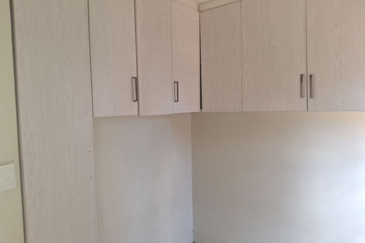 A compact kitchen area featuring light wood-finish built-in cabinetry and tiled flooring, presenting a clean but dated space ready for updates.
