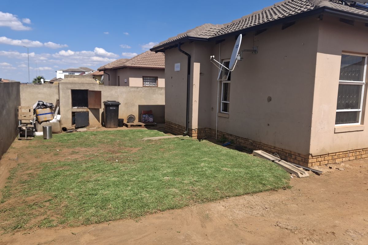 Rear exterior view of the property featuring a small lawn, built-in braai, and solar water heating system installed on the tiled roof.