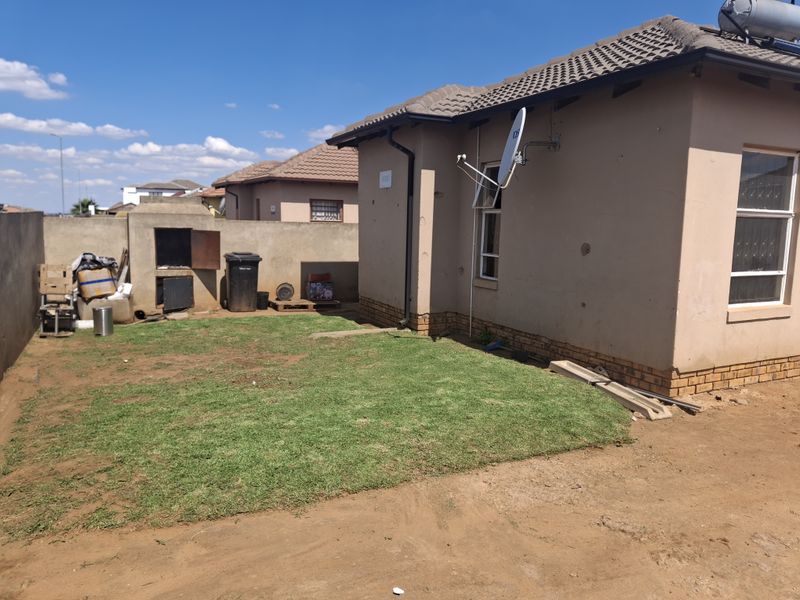 Rear exterior view of the property featuring a small lawn, built-in braai, and solar water heating system installed on the tiled roof.