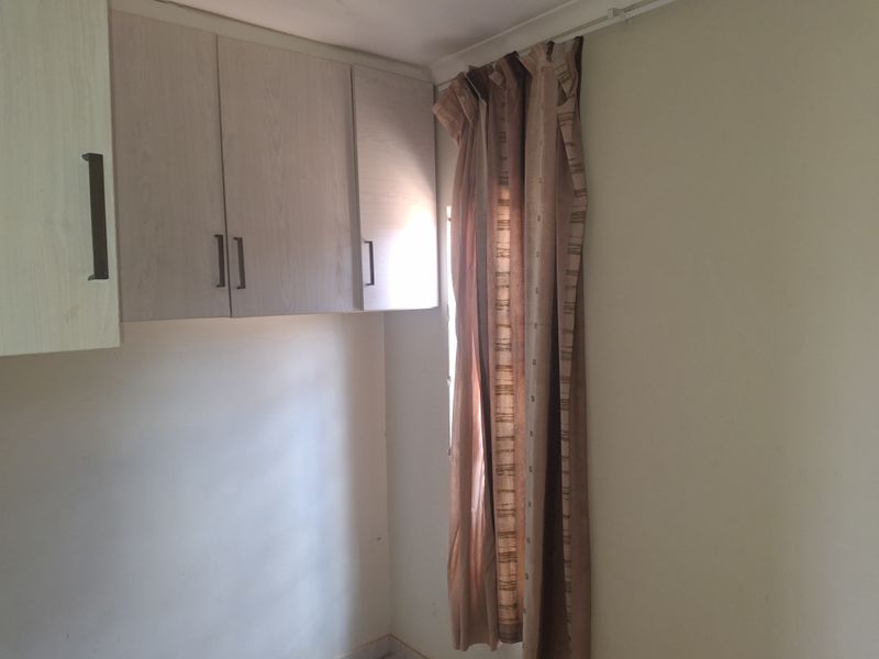A bedroom corner featuring built-in wall-mounted cabinetry and a window with a curtain rail.