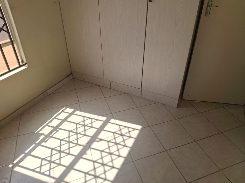 A vacant bedroom featuring built-in cupboards, tiled flooring, and a window with security bars, offering a clean canvas for personalization.