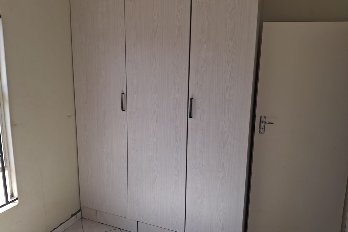 A bedroom featuring built-in wardrobes with light wood-grain finish and tiled flooring.