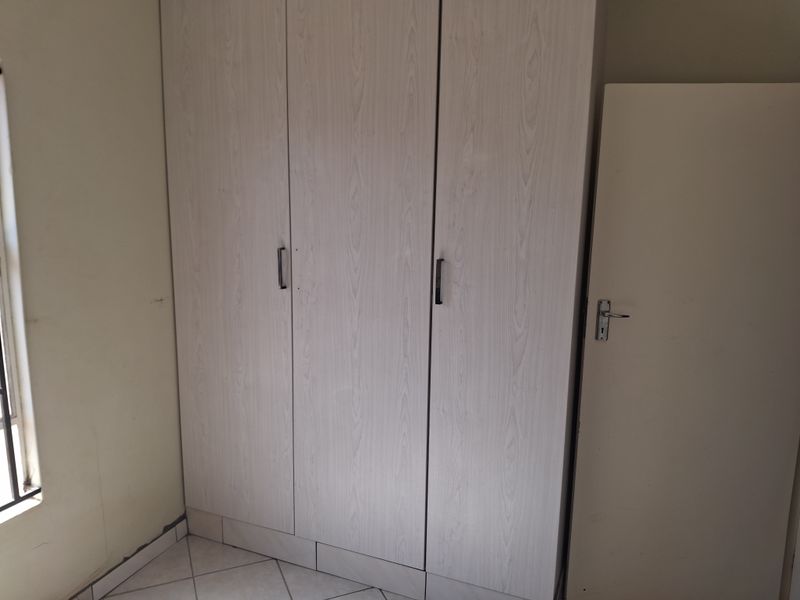 A bedroom featuring built-in wardrobes with light wood-grain finish and tiled flooring.
