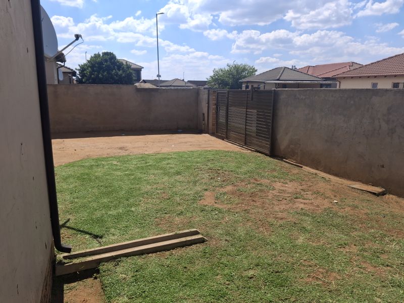 A rear yard featuring a perimeter wall, metal sliding gate, and a mix of lawn and bare soil, offering potential for landscaping improvements.