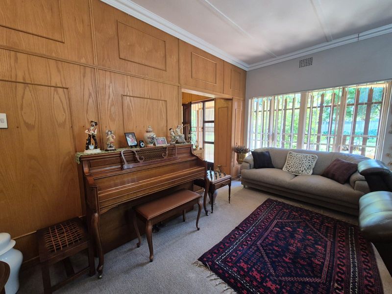 A living room featuring classic wood wall paneling, crown molding, and large windows with vertical blinds, offering a traditional aesthetic.