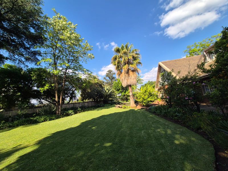 A spacious rear garden featuring a well-maintained lawn, mature trees, and a view of the property's brick exterior and tiled roof.