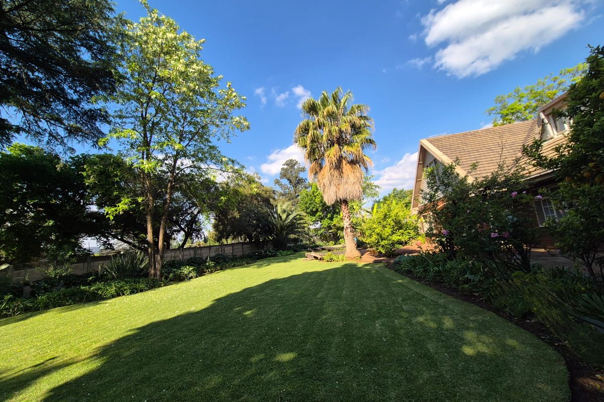 A spacious rear garden featuring a well-maintained lawn, mature trees, and a view of the property's brick exterior and tiled roof.