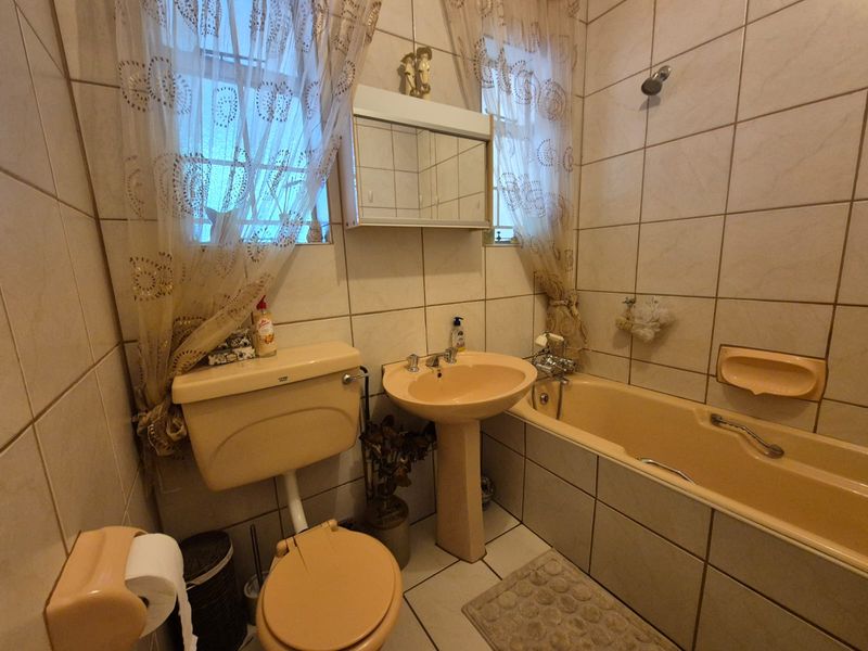 A compact bathroom featuring a dated peach-colored suite, including a pedestal basin, bathtub, and toilet, finished with neutral wall and floor tiling.