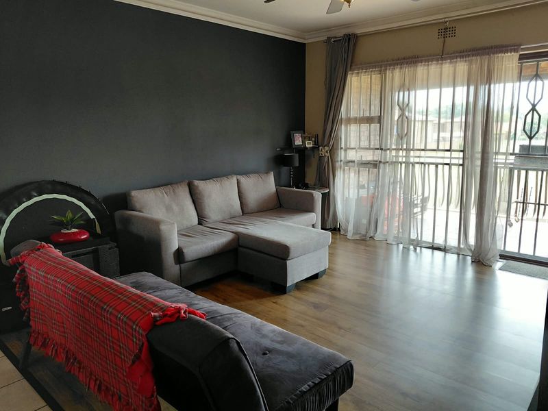 A living room featuring laminate flooring, a dark accent wall, and a sliding glass door with security gate leading to an outdoor area.
