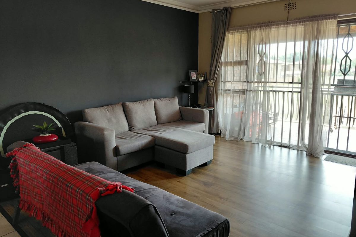 A living room featuring laminate flooring, a dark accent wall, and a sliding glass door with security gate leading to an outdoor area.