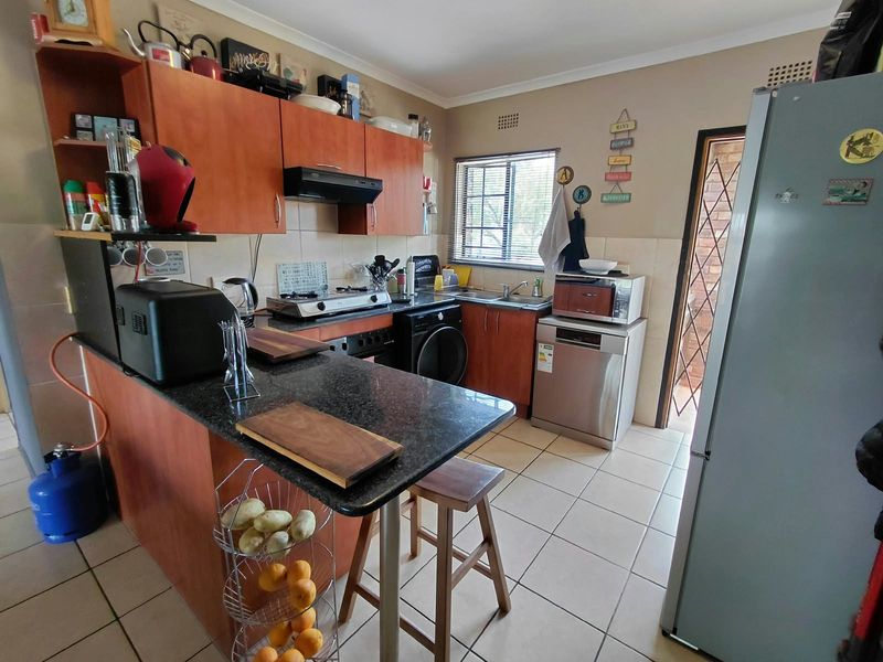 Functional kitchen featuring wooden cabinetry, granite countertops, gas hob, and tiled flooring with direct access to an exterior area.
