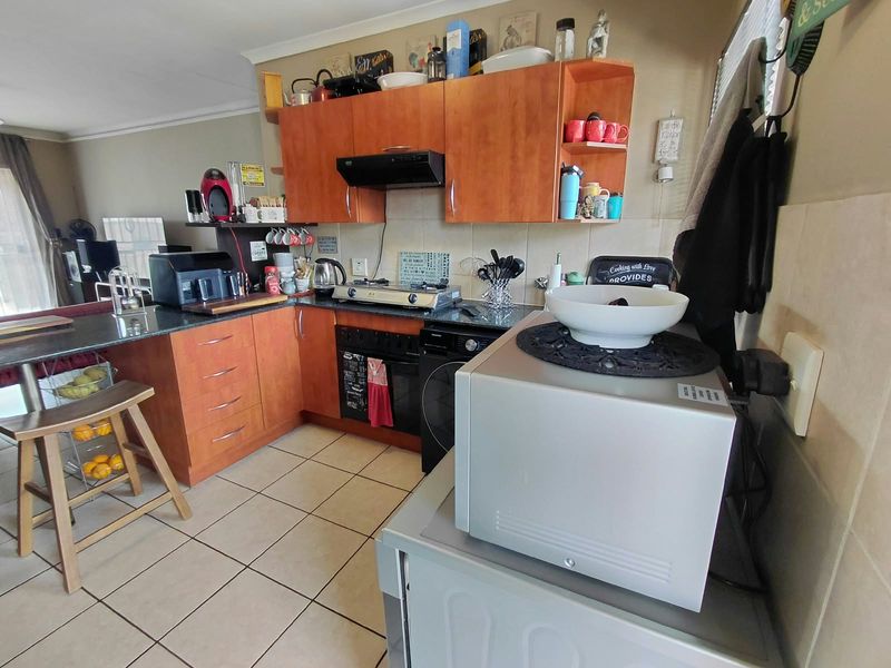 A functional kitchen featuring wooden cabinetry, granite countertops, a gas hob, and tiled flooring, offering a practical layout for daily meal preparation.