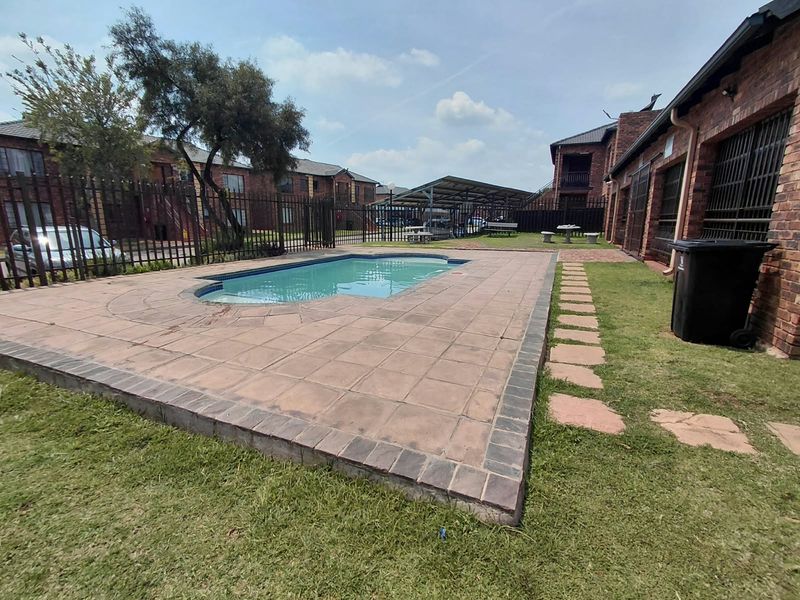 Communal outdoor pool area featuring a paved deck, metal perimeter fencing, and brick townhouse exterior walls within a residential complex.
