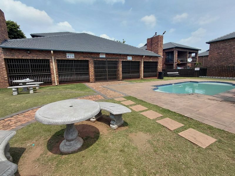 Communal pool area featuring a paved deck, brick building facade with security gates, and landscaped garden space with stone pathways.