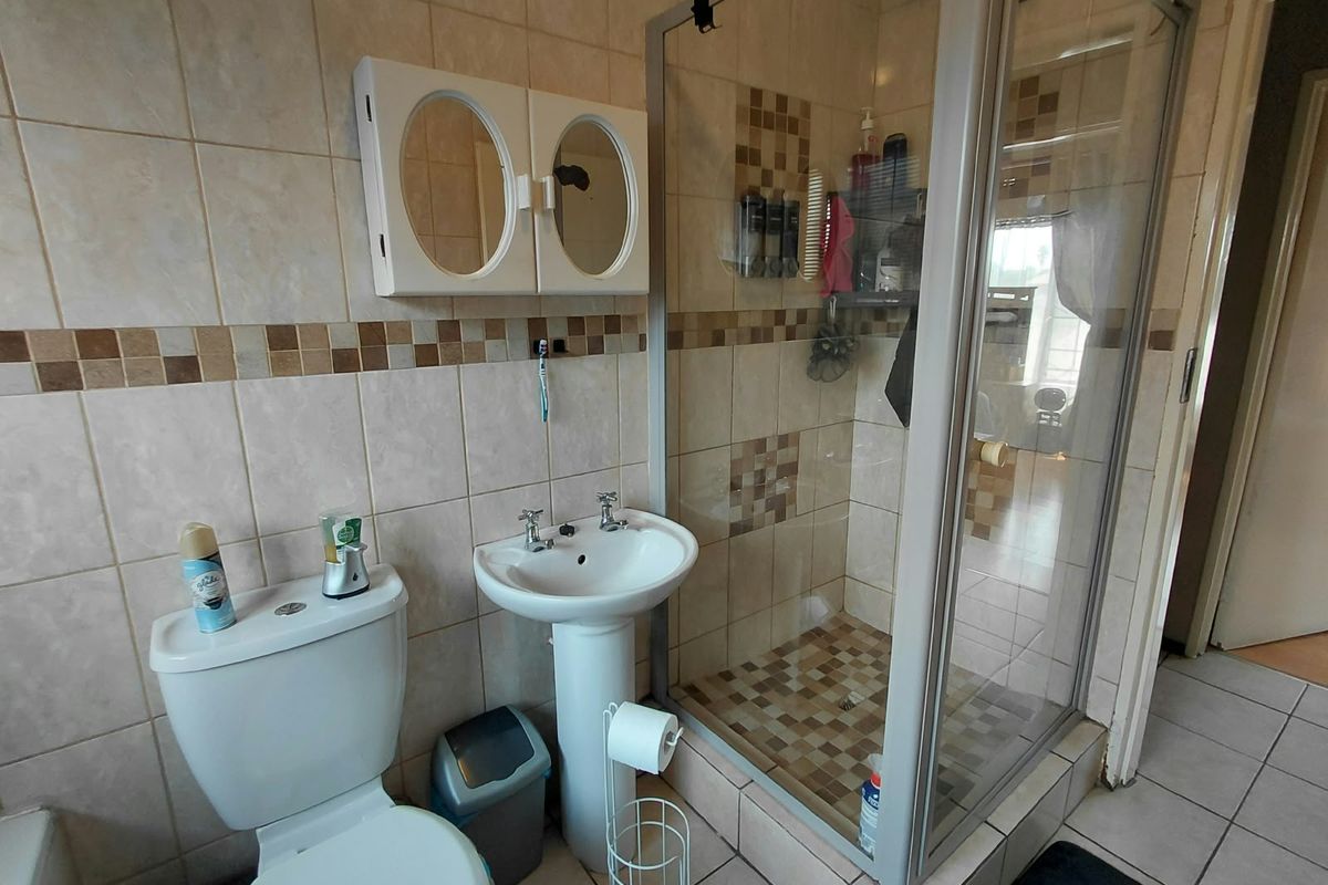 A functional bathroom featuring a pedestal basin, a glass-enclosed shower, and neutral ceramic tiling throughout.