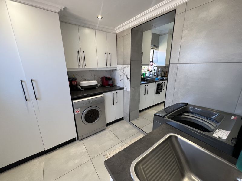 A functional scullery featuring modern built-in cabinetry, tiled finishes, and a stainless steel sink, providing additional workspace and utility storage.