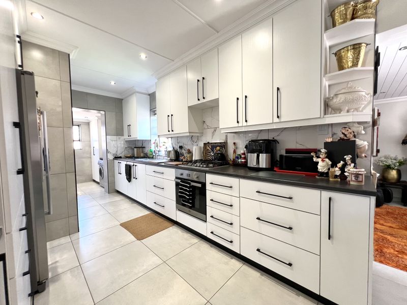 Modern kitchen featuring white cabinetry, dark stone countertops, built-in oven and gas hob, complemented by large format floor tiles and marble-look splashback.