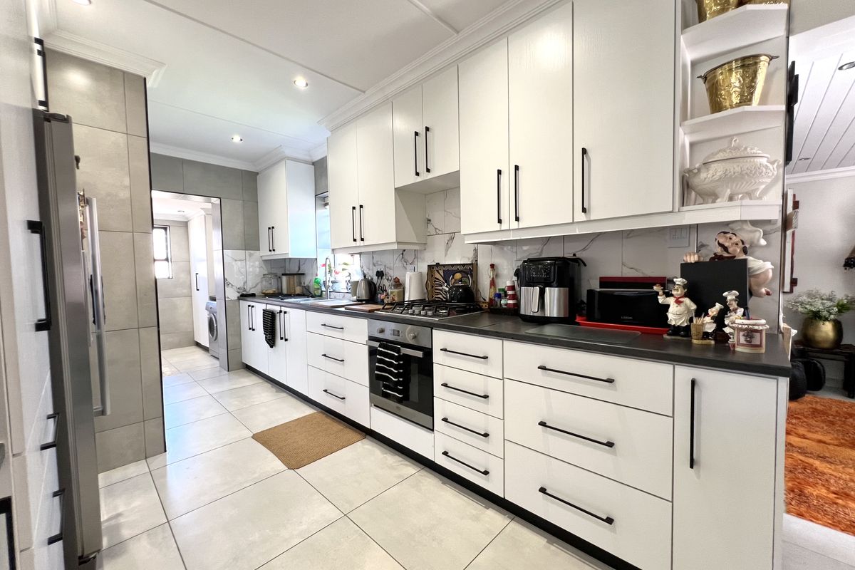 Modern kitchen featuring white cabinetry, dark stone countertops, built-in oven and gas hob, complemented by large format floor tiles and marble-look splashback.