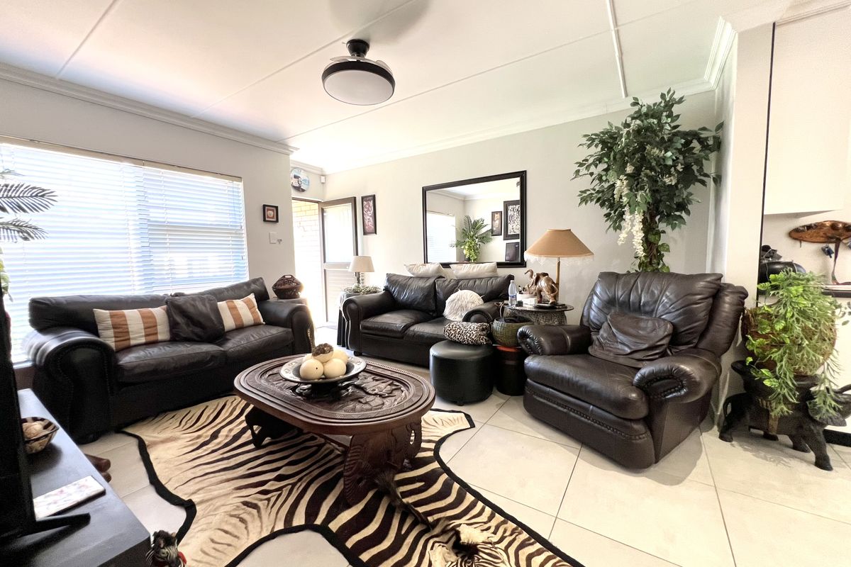 A spacious living room featuring large format floor tiles, a ceiling fan, and natural light provided by windows with venetian blinds.