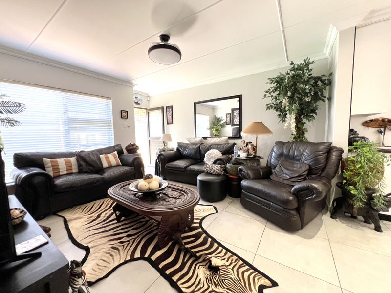 A spacious living room featuring large format floor tiles, a ceiling fan, and natural light provided by windows with venetian blinds.