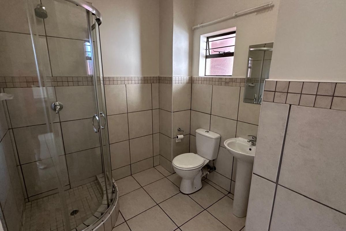 A functional bathroom featuring a curved glass shower enclosure, pedestal basin, toilet, and neutral tiled finishes throughout.