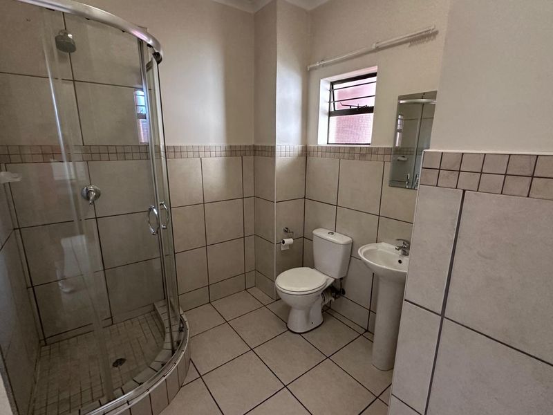 A functional bathroom featuring a curved glass shower enclosure, pedestal basin, toilet, and neutral tiled finishes throughout.