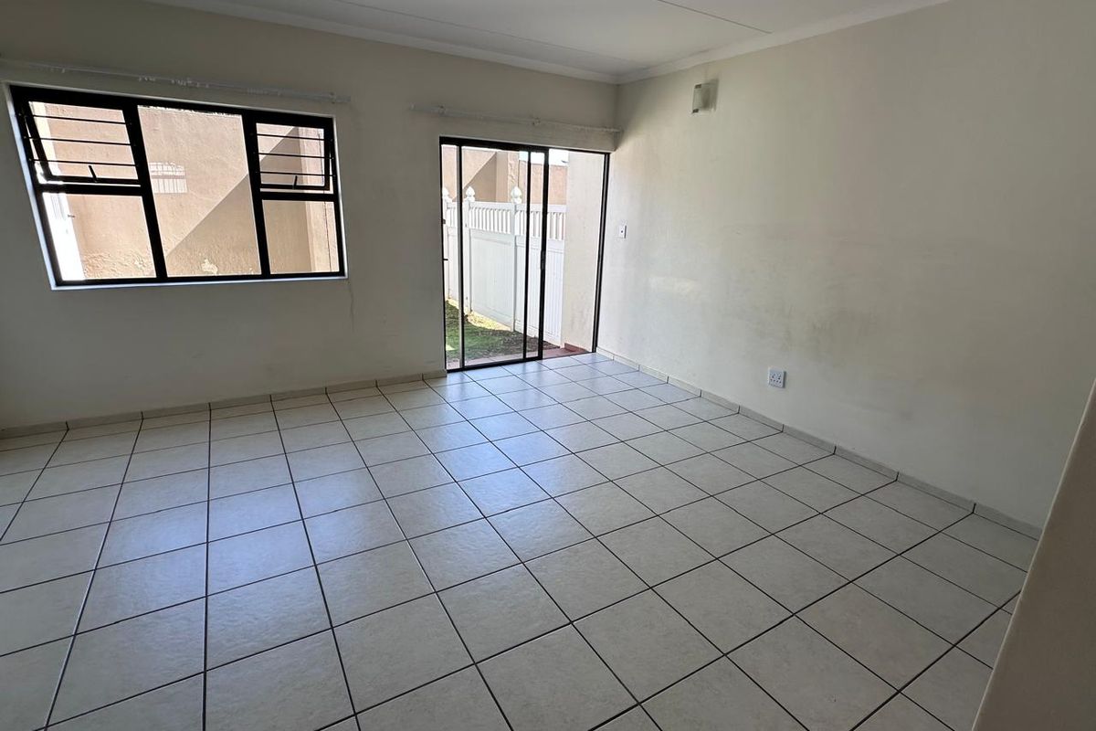 An empty, tiled living room featuring large windows and a sliding glass door providing access to the exterior.
