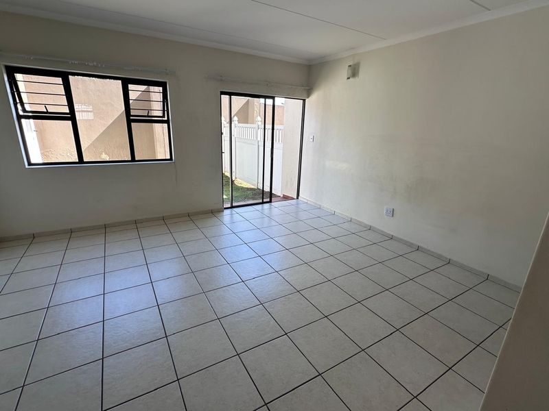 An empty, tiled living room featuring large windows and a sliding glass door providing access to the exterior.