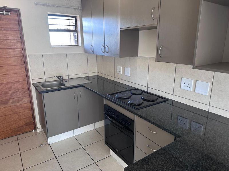 A compact, functional kitchen featuring modern grey cabinetry, granite countertops, a built-in oven and hob, and neutral tiled finishes.