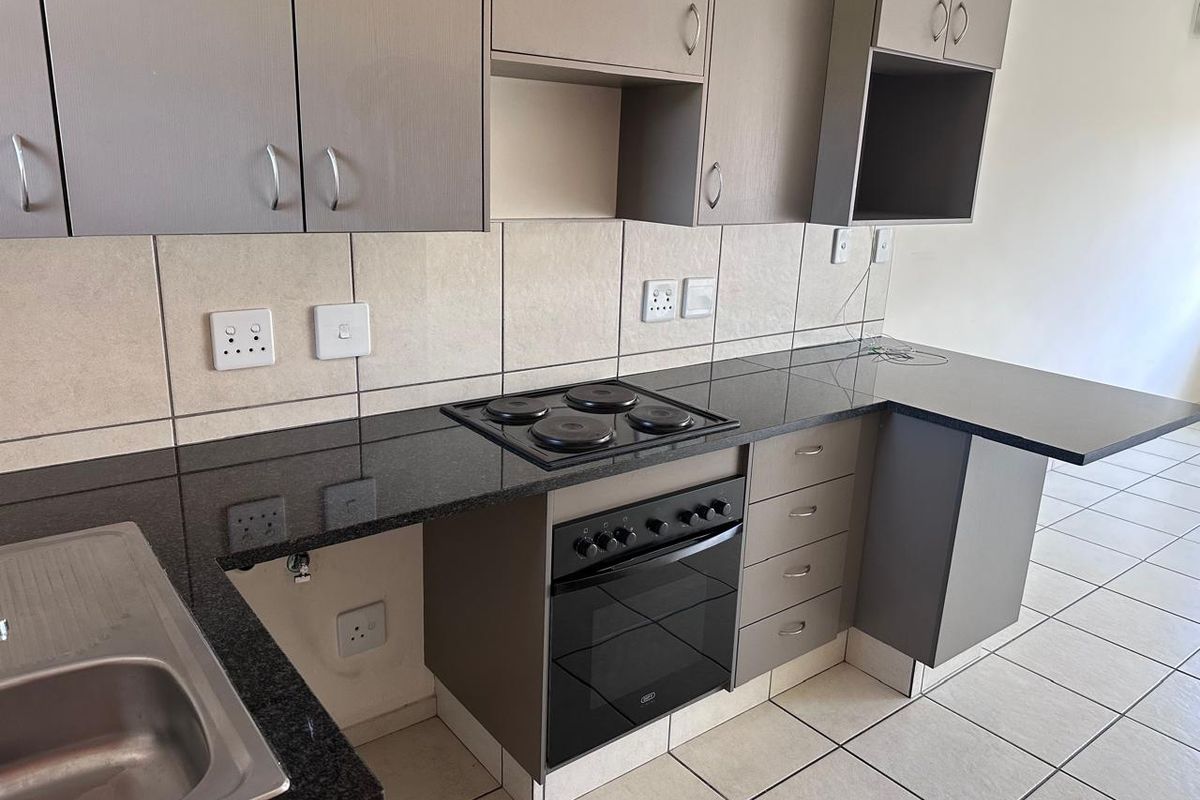 Modern kitchen featuring granite countertops, built-in oven and hob, ample cabinetry, and tiled finishes, presenting a clean and functional workspace.