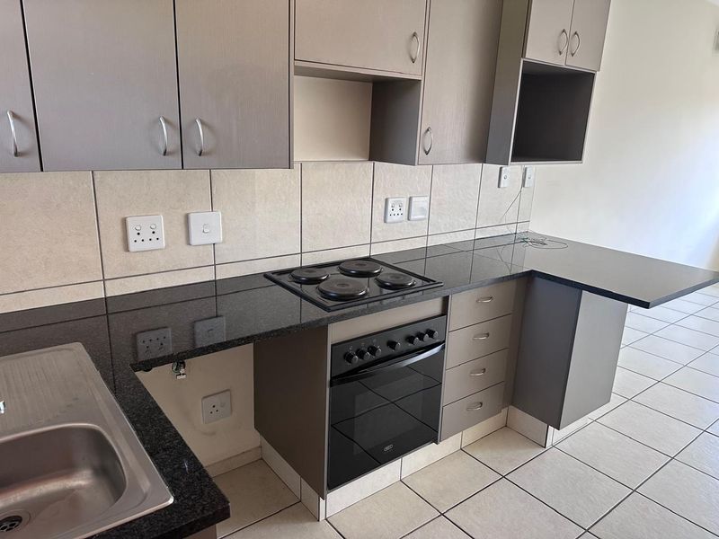 Modern kitchen featuring granite countertops, built-in oven and hob, ample cabinetry, and tiled finishes, presenting a clean and functional workspace.