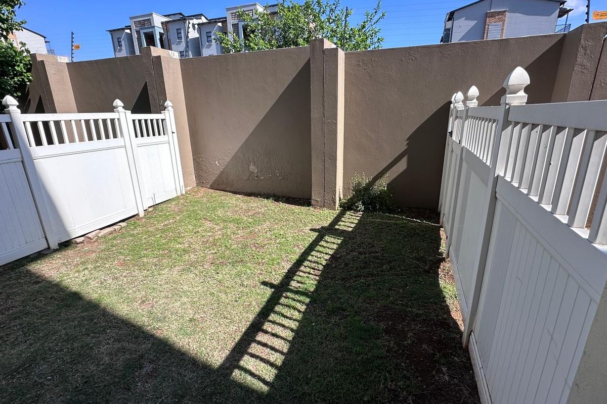 A private rear garden area featuring a small lawn enclosed by white vinyl fencing and a solid boundary wall.