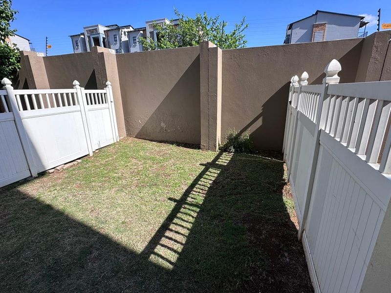 A private rear garden area featuring a small lawn enclosed by white vinyl fencing and a solid boundary wall.