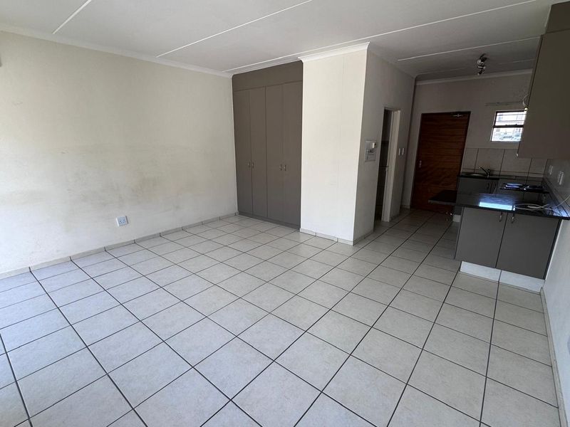 Open-plan living area featuring tiled flooring, built-in cupboards, and an adjoining kitchen with granite countertops and fitted cabinetry.