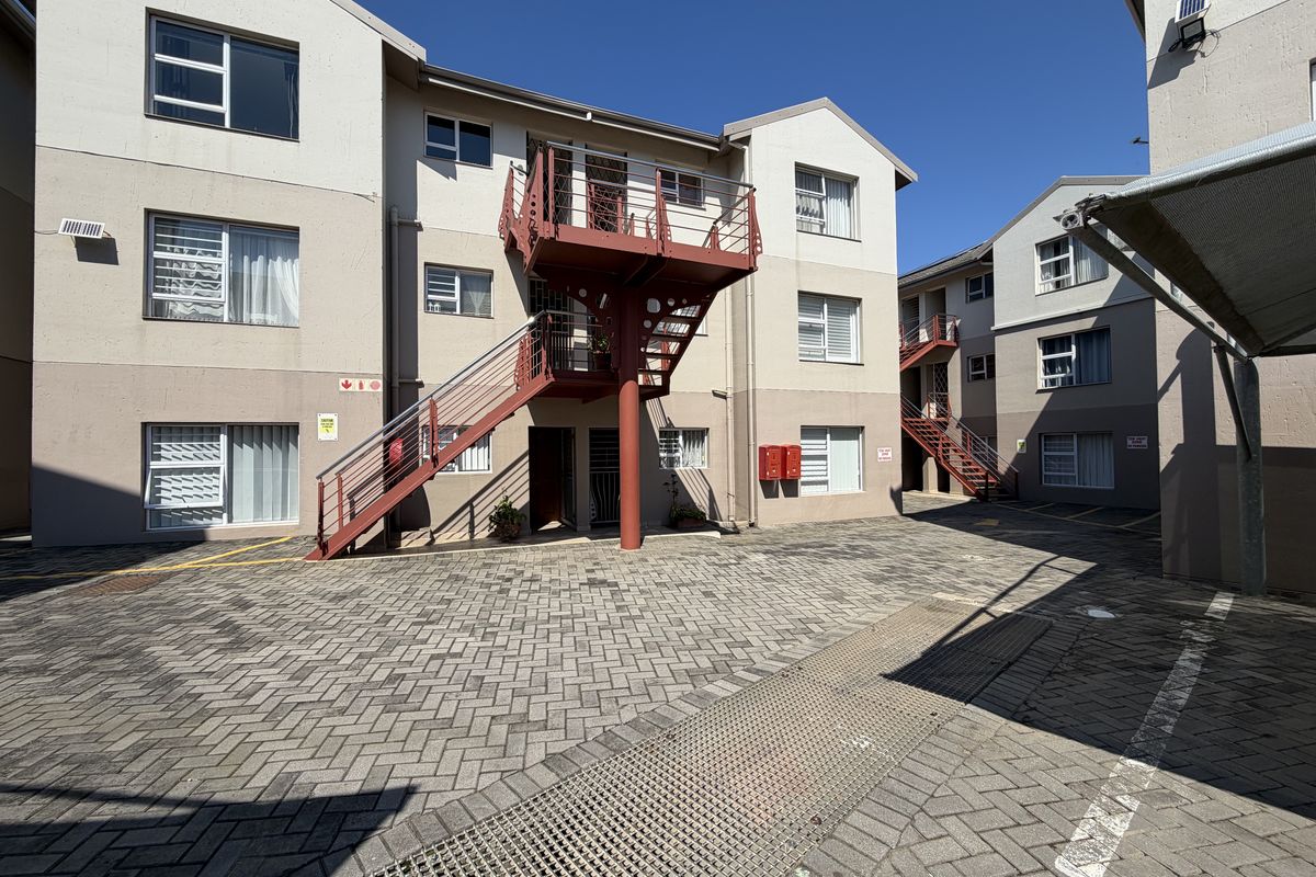 Exterior view of an apartment complex featuring paved parking areas, metal staircases, and communal balconies.