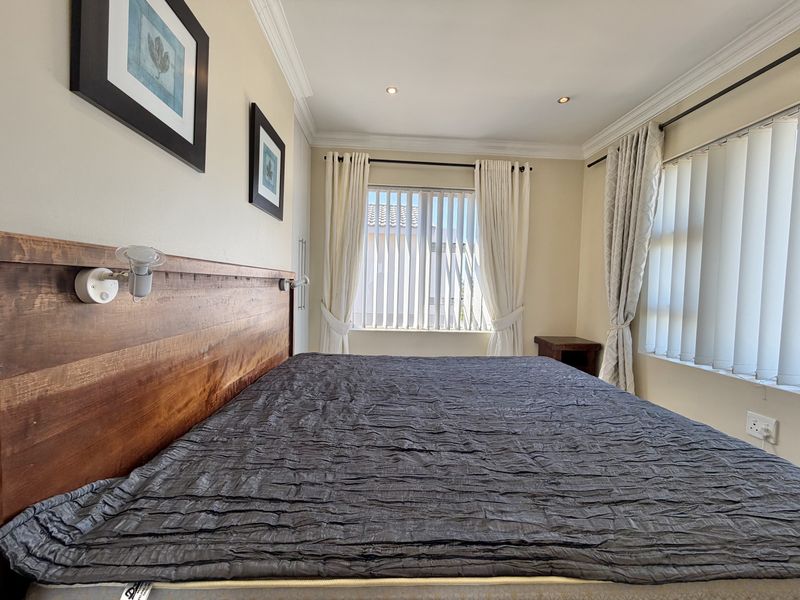 A well-maintained bedroom featuring recessed downlights, crown molding, and dual window treatments including vertical blinds and curtains.