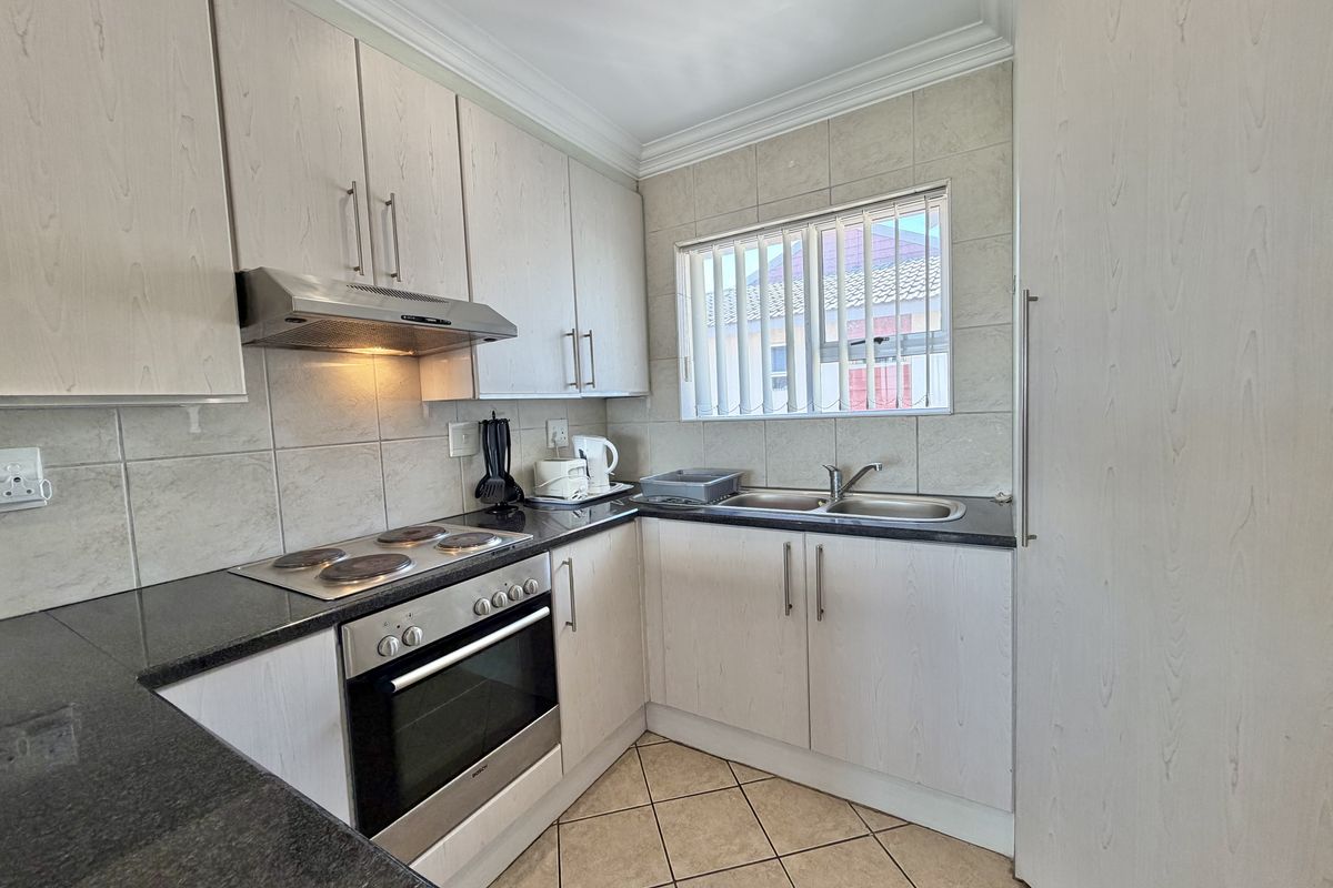 A functional kitchen featuring light wood-finish cabinetry, granite countertops, a built-in oven with hob, and a double basin sink with tiled backsplash.