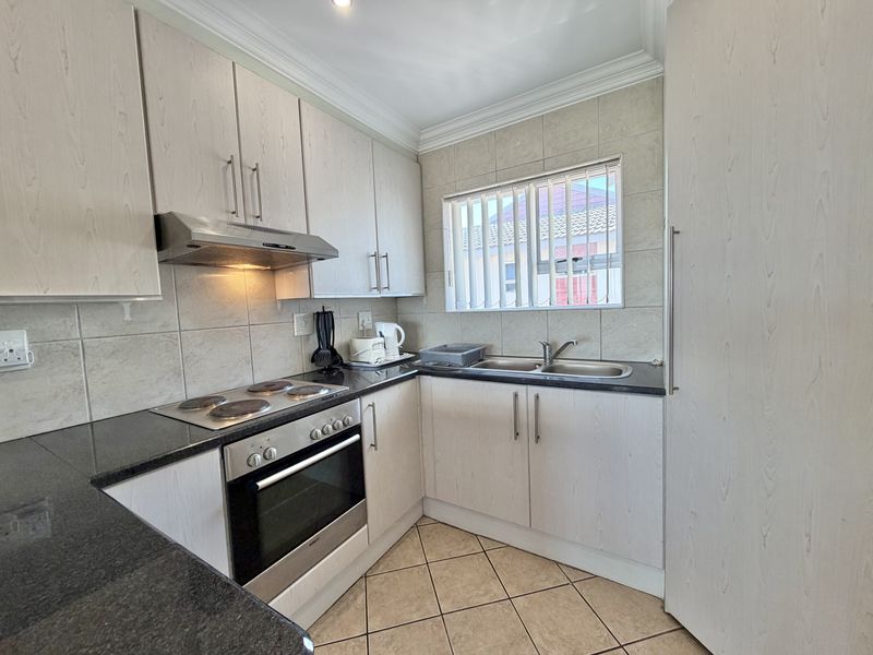 A functional kitchen featuring light wood-finish cabinetry, granite countertops, a built-in oven with hob, and a double basin sink with tiled backsplash.