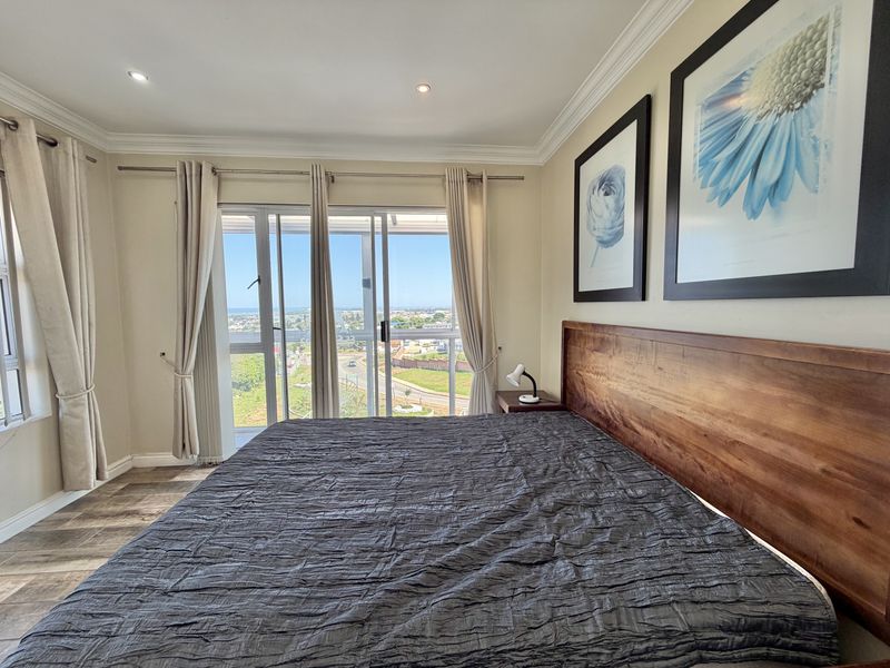 A well-maintained bedroom featuring laminate flooring, crown molding, recessed lighting, and large sliding glass doors that provide natural light and scenic views.