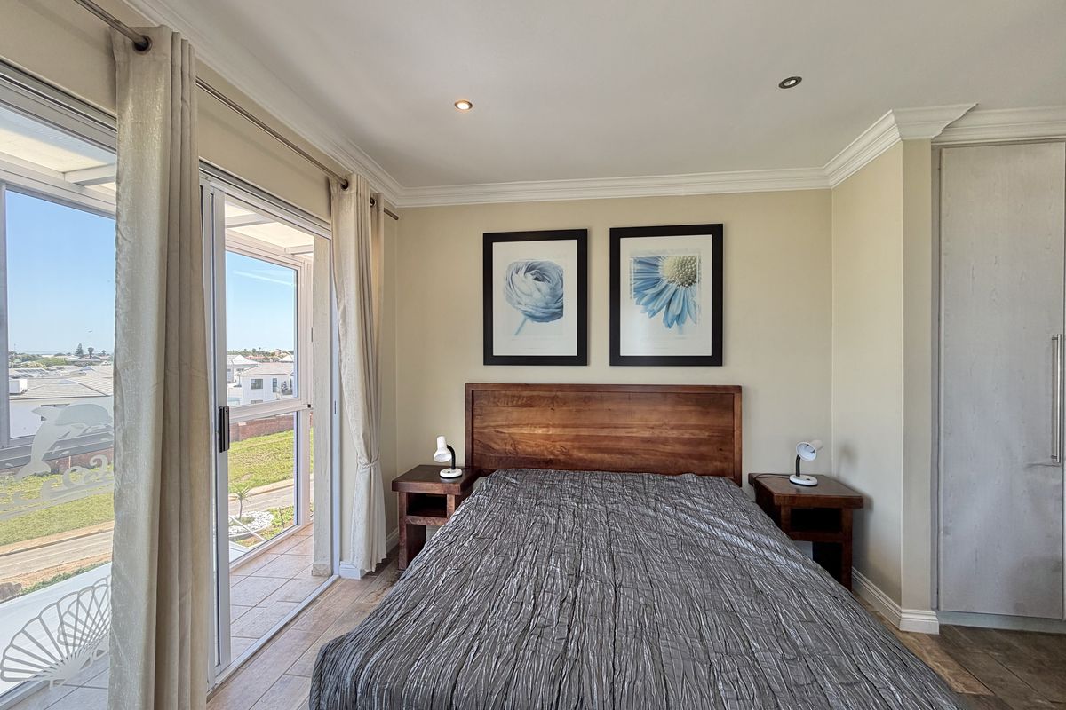 A well-maintained bedroom featuring tiled flooring, recessed lighting, crown molding, and a sliding glass door providing access to a balcony with neighborhood views.