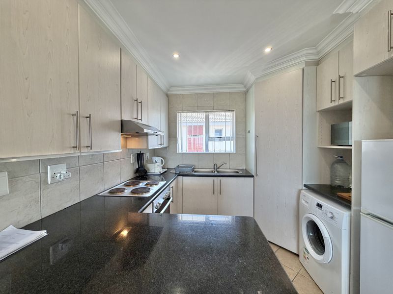 A functional kitchen featuring light wood cabinetry, granite countertops, an electric hob, built-in oven, and dedicated space for a washing machine.