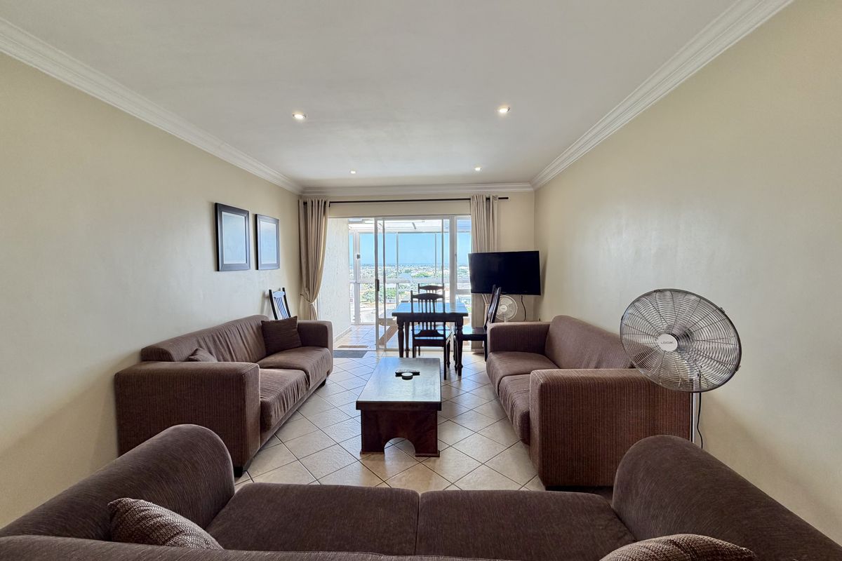 A spacious living room featuring tiled flooring, recessed downlighting, and a sliding glass door that opens to a balcony with scenic views.