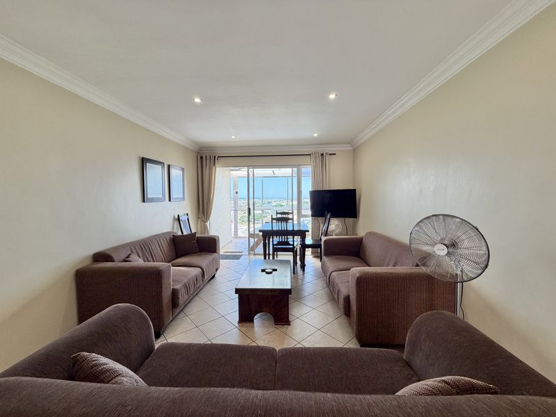 A spacious living room featuring tiled flooring, recessed downlighting, and a sliding glass door that opens to a balcony with scenic views.