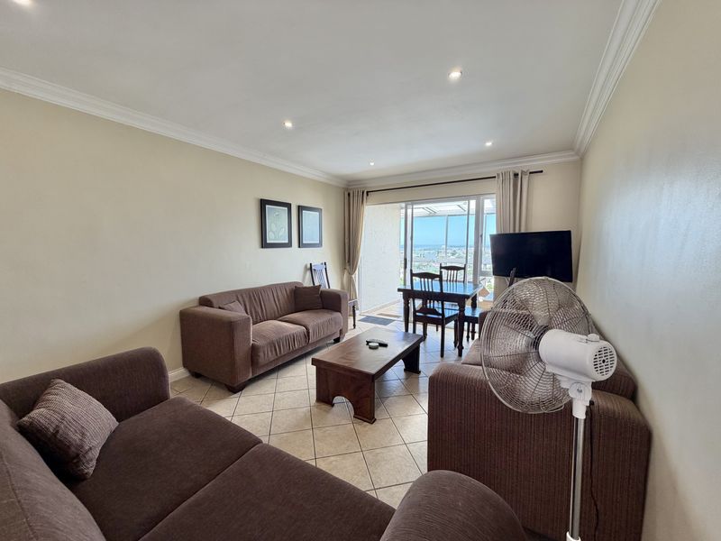 Open-plan living and dining area featuring tiled flooring, recessed lighting, and sliding glass doors leading to a balcony with coastal views.